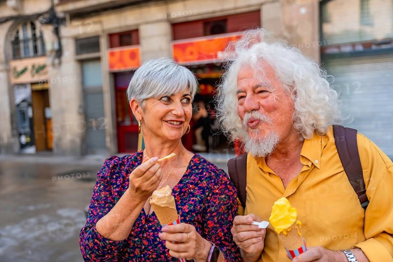 Happy senior couple eating ice cream cones while walking on a city street, sharing a sweet moment together during their urban exploration and leisure time