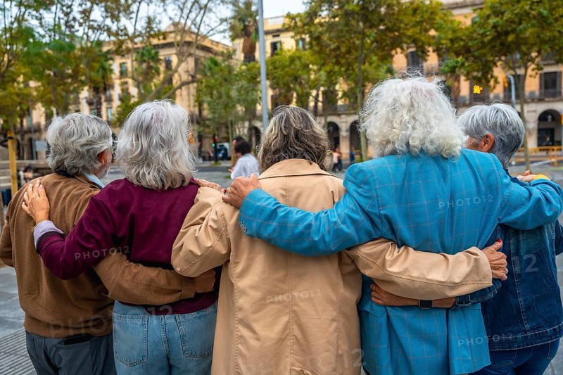 Group of diverse seniors walking together in a city, embracing with arms around each other, demonstrating strong friendship, support, and a sense of community outdoors
