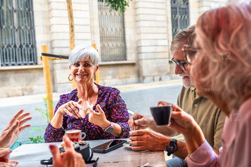 Mature adults gathering socially at an outdoor cafe, enjoying coffee and engaging in lively conversation, representing retirement, friendship, and a happy lifestyle