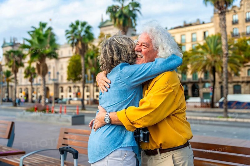 Enthusiastic senior couple embracing each other with joy and affection in a city setting, enjoying travel and leisure together on an urban street with palm trees