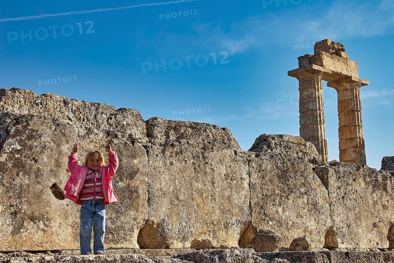 Child standing in front of an ancient column. Stones and sky in the background, Nemea, Ancient Zeus Church, Archeological Site, Peloponnese, Greece