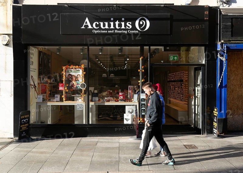 Shoppers passing Acuitis opticians and hearing centre shop store, High Street, Exeter, Devon, England, UK