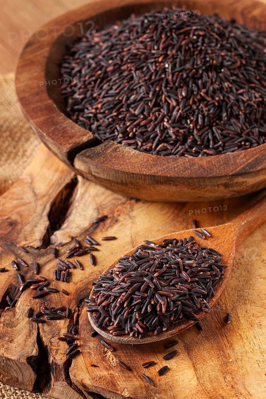 Natural black rice in a wooden bowl and spoon on a wooden surface in rustic style, top view