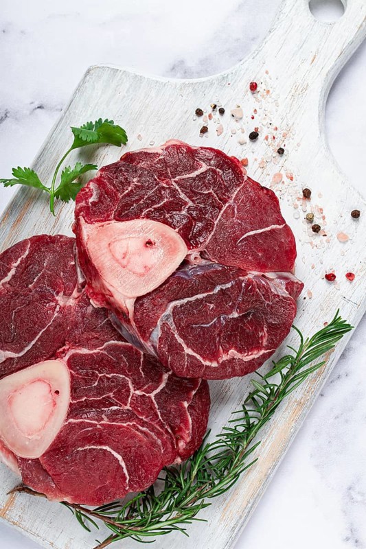 Knuckle on the bone, raw meat for ossobuco, on a wooden chopping board, with a sprig of rosemary, and spices, top view, no people
