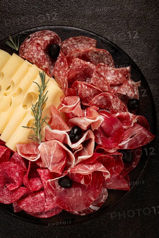 Cold cuts, appetizer, prosciutto, salami and ham, with maasdam cheese and olives, on a round plate, breakfast, top view, close-up, deserted