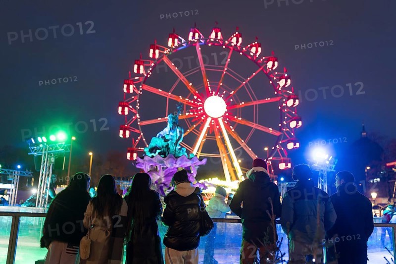 Several people watch ice skaters in front of the Neptune Fountain and a Ferris wheel at the Berlin Christmas market on Alexanderplatz, Berlin, 24.11.2025