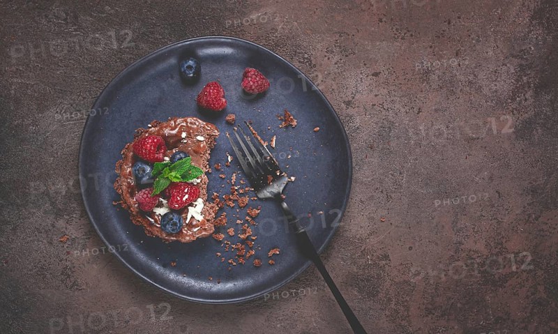 Half-eaten chocolate tartlet, on a plate, stuffed with cottage cheese and berries, breakfast, homemade, no people