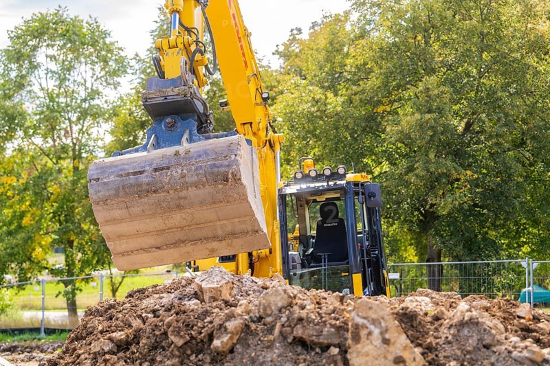 An excavator on a construction site lifts soil near trees and a cloudy sky, building a PV open air system, Weil der Stadt, Germany
