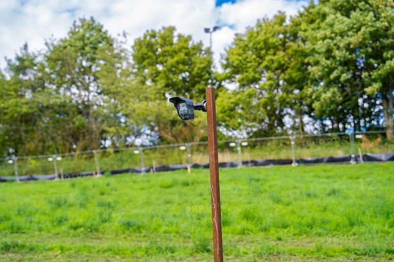 Camera on a post with grass and trees in the background under a blue sky, Bau PV Freifaechenanlage, Weil der Stadt, Germany