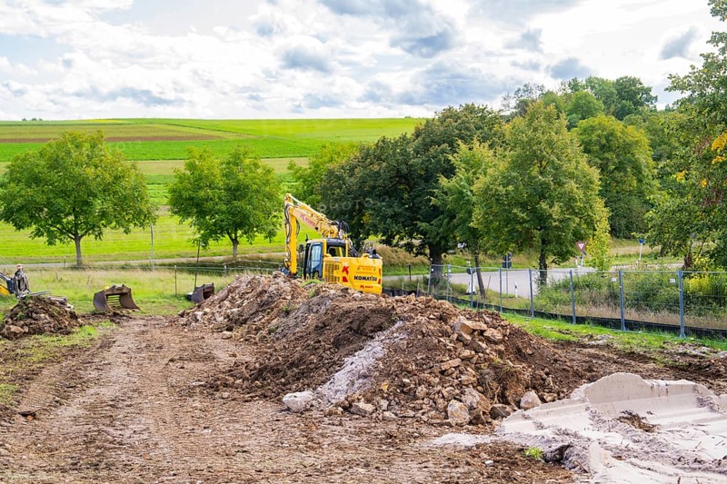 Excavator on a construction site with large mounds of soil in a green landscape, Bau PV Freifaechenanlage, Weil der Stadt, Germany