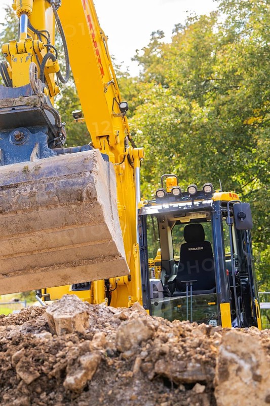 Close-up of an excavator with a raised grab arm at a construction site in front of trees, PV Freifaechenanlage construction, Weil der Stadt, Germany