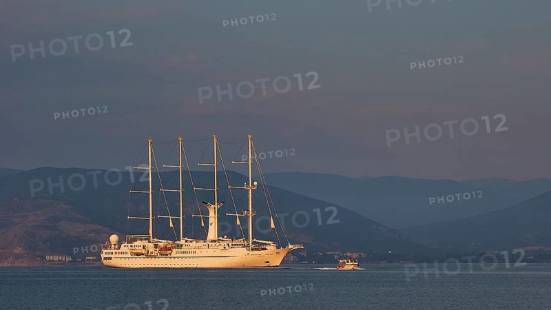 An illuminated sailing ship on calm water with mountains in the background at dusk, Nauplion, Nafplion, Peloponnese, Greece