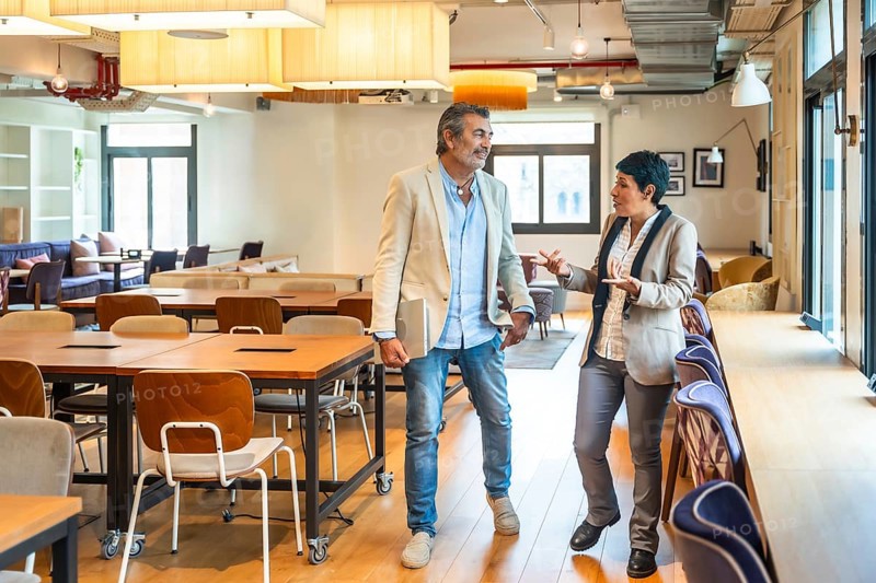 Diverse business professionals walking, talking, and discussing work in an open plan office, highlighting teamwork, innovation, and a dynamic corporate environment