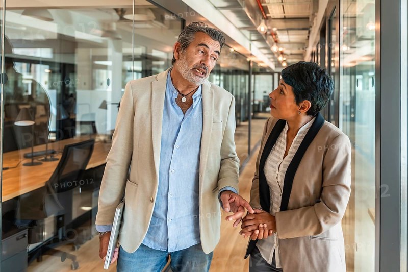 Mature business colleagues walking down a modern office corridor, having an engaging discussion and exchanging ideas during an informal meeting in a coworking space