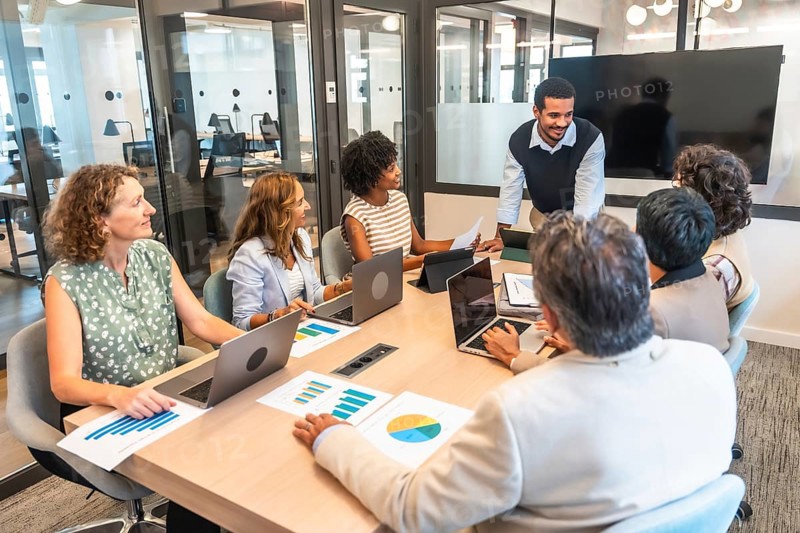 Diverse business professionals conducting a collaborative meeting in a modern office, analyzing data and discussing strategy, representing teamwork and corporate success