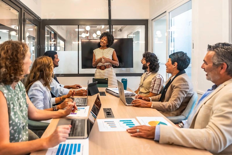 Diverse business professionals sharing ideas, discussing strategy, and presenting data during a corporate meeting in a modern coworking office, fostering collaboration and teamwork