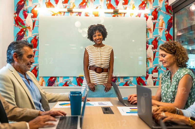 Diverse business team collaborating in a vibrant coworking space, discussing data charts and laptops while a confident presenter leads strategy, brainstorming and planning for success