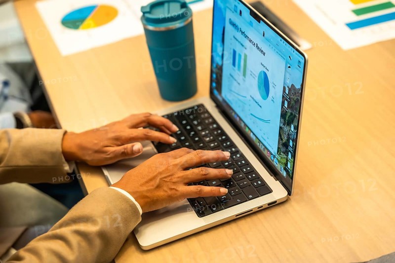 Person working on a laptop, hands typing on the keyboard, with a monthly performance review screen showing charts and graphs, indicating data analysis and business operations