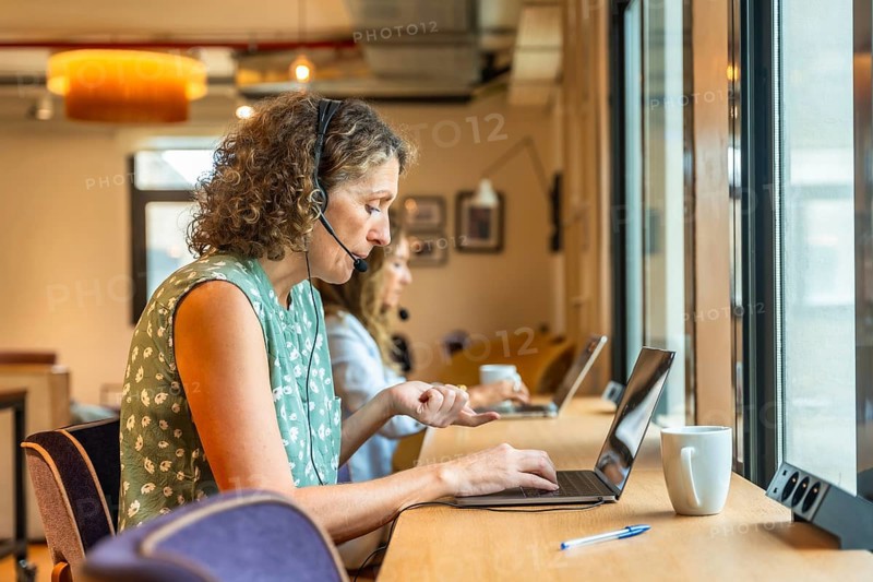 Women concentrating on their work using laptops and headsets in a modern coworking office, demonstrating remote teamwork and professional communication