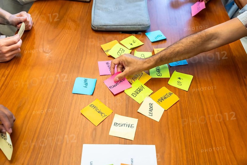 Business team gathered around wooden table arranging colorful sticky notes labeled planning. Marketing. Energy and efficiency. Collaborating on strategy. Creativity and problem solving during meeting