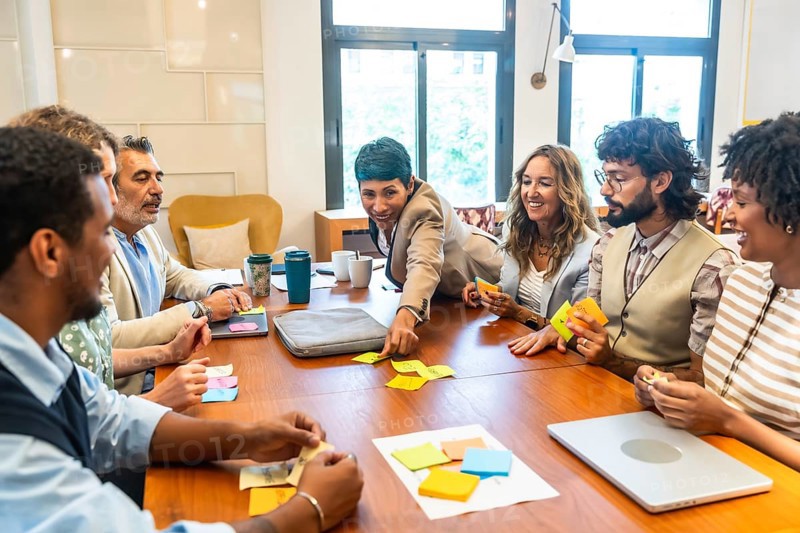 Diverse business team collaborating energetically around a table, exchanging ideas, brainstorming with sticky notes and laptops in a modern office to solve problems and plan strategy