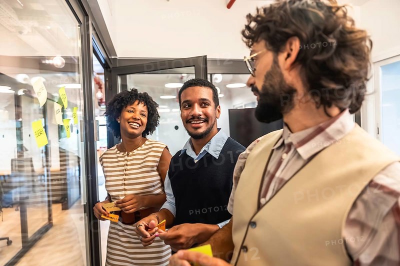 Diverse business professionals collaborating happily, exchanging creative ideas, and planning effectively during an engaging team meeting with sticky notes on a glass wall in an modern office