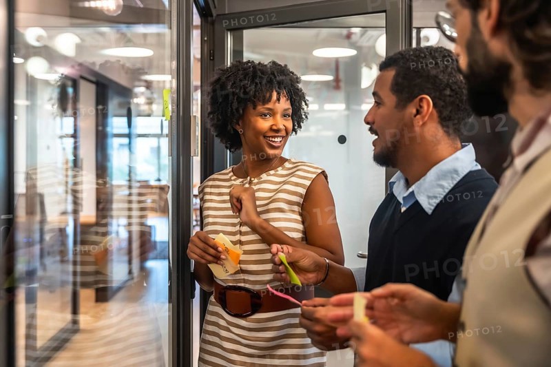 Diverse business people collaborating during an agile meeting, discussing creative concepts and sharing thoughts with colorful sticky notes on a glass office wall