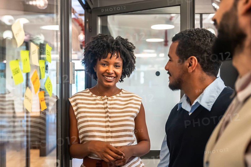 Smiling african american woman presenting ideas while discussing project strategies with diverse team members during a corporate brainstorming session in a coworking space