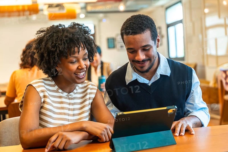 Diverse young business colleagues are enjoying a teamwork moment, looking at a digital tablet together and discussing content in a modern coworking office environment
