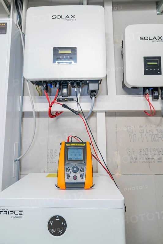 PVCheck PRO in front of installed Solax devices with red cable connections