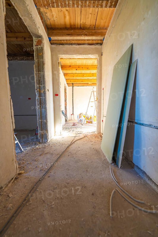 A shell with sunlight in the corridor. Cables, unfinished walls and a wooden floor define the room