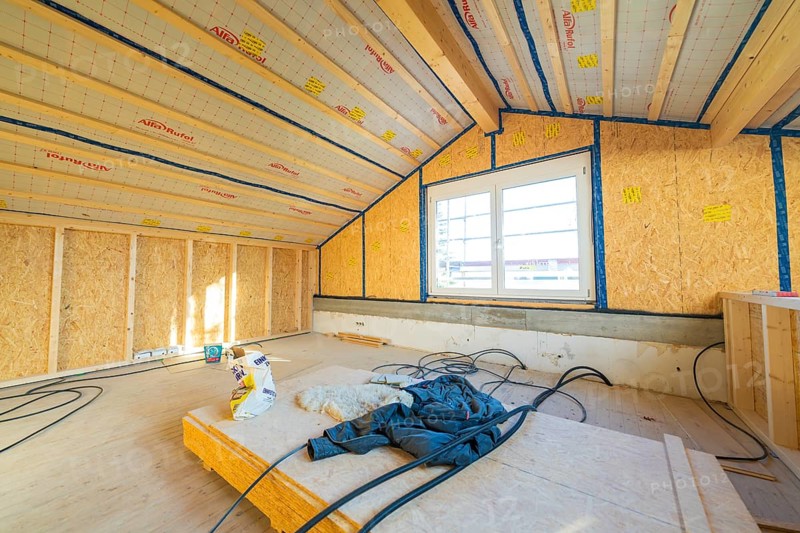Unfinished construction of an attic with insulation on the walls. Large windows let in lots of light