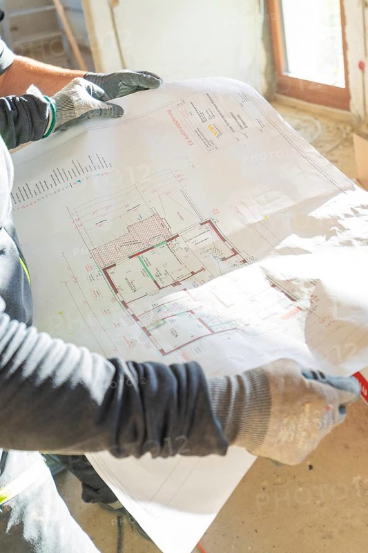 A construction worker holds a construction plan in his hands in a light-filled room