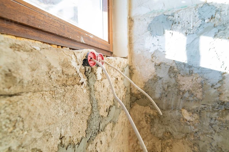 Cables hang loose from an unfinished wall, next to windows during renovation