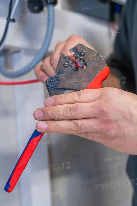 Electrician processes cables with pliers, workshop environment