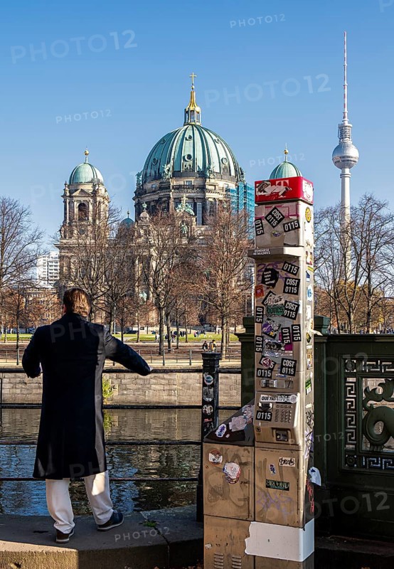 A man stands next to a demolished modern Telekom telephone column, view of Lustgarten Cathedral, Berlin, Germany