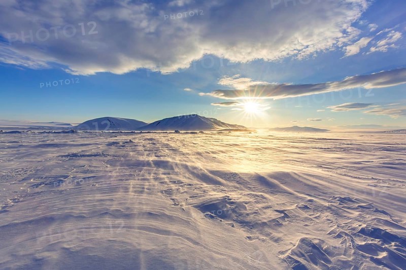 Midnight sun over windswept snow covered Arctic landscape at Mohnbukta, bay at western shore of Storfjorden in Sabine Land, Spitsbergen, Svalbard