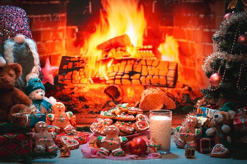 A plate of cookies and a glass of milk next to a Christmas tree and toys in front of a fireplace