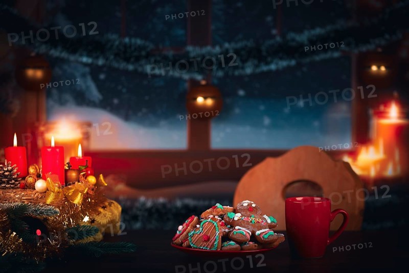 Festively decorated table with candles and cookies in front of a snowy window at night