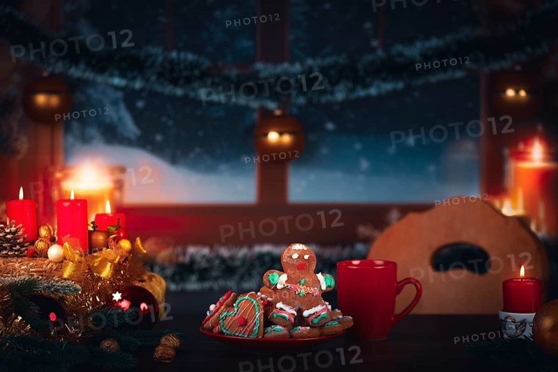 Christmas wreath with burning candles next to a plate with gingerbread in front of a window