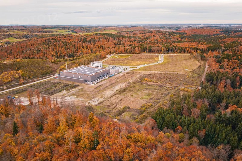 Industrial plant surrounded by autumnal forest with fields and roads in the background, new Lindenrain industrial park, Calw, Black Forest, Germany
