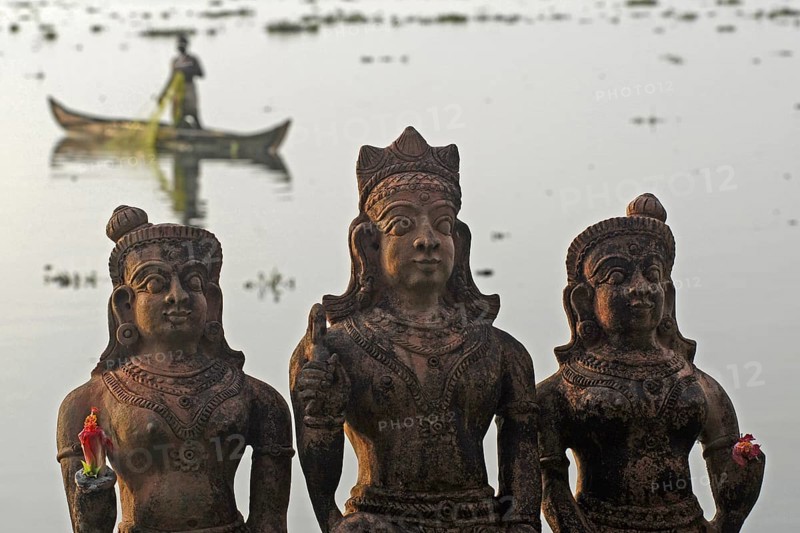 Three Hindu god statues made of clay, fishermen in a boat in the background, Vembanad Lake, Kerala, India
