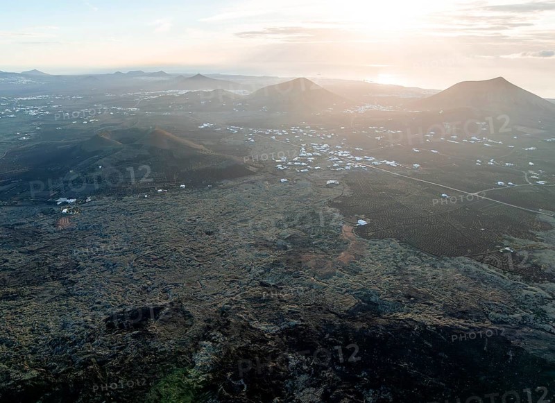 Picturesque volcanic landscape with volcanic craters and lava fields in the morning light, white houses in the village of Masdache, Parque Natural de Los Volcanes, aerial view, Lanzarote, Canary Islands, Spain
