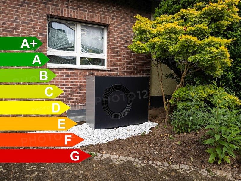 A black heat pump in a front garden, graph with energy efficiency classes for buildings according to the GEG, Hilden, Germany