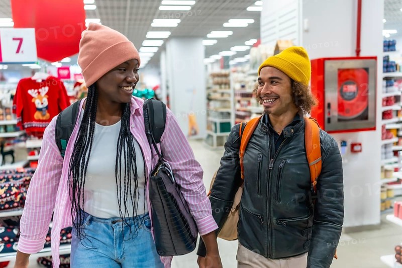 Diverse young couple smiling while holding hands, walking together down an aisle in a retail store during holiday shopping for christmas presents and decorations