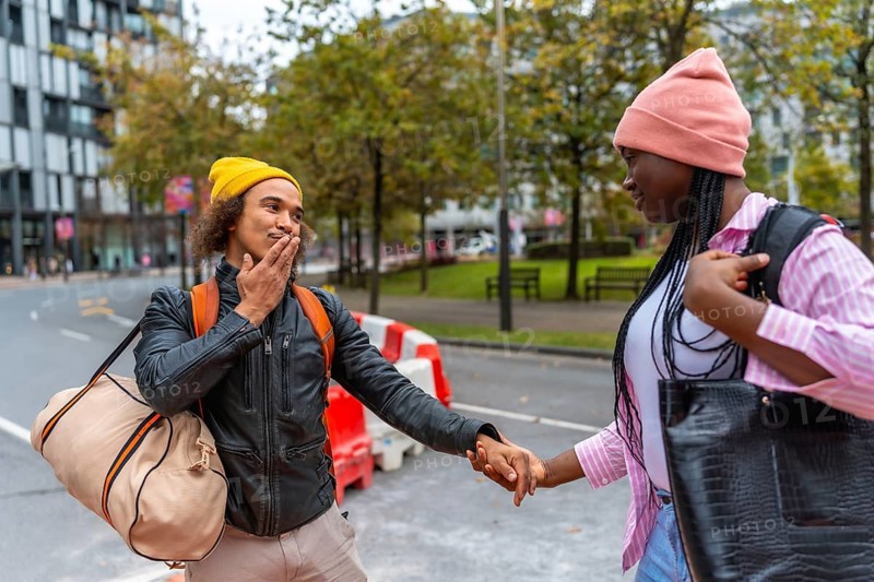 Young diverse couple holding hands while walking on an urban street, exploring the city together with bags and backpacks, representing travel and relationship