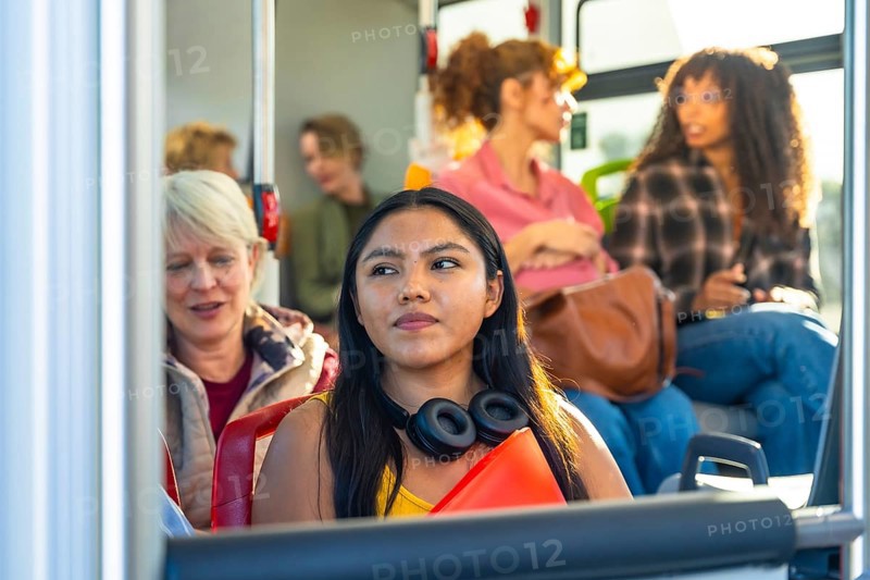 Young woman looking away while commuting on a bus with a diverse group of passengers, representing urban travel and daily life for people relying on public transportation