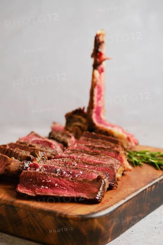 Thick slices of perfectly cooked t-bone steak medium rare on a wooden cutting board. Fresh herbs add a touch of green to the rustic scene