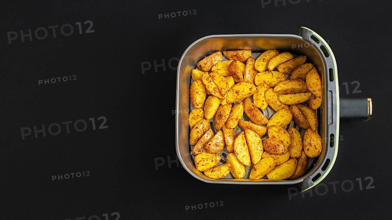 Top view of golden brown potato wedges in an air fryer basket against a dark background. These deliciously seasoned wedges are perfect for snacking or as a side dish at any meal time