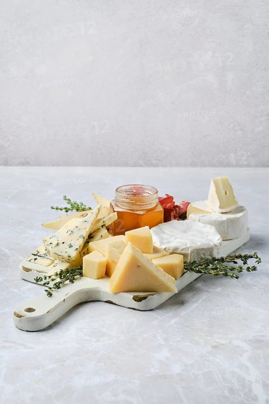 Fine selection of cheeses, honey, and herbs arranged artfully on a platter. Cubes of aged cheese, soft rounds, and honey jar create a tempting display, ideal for gatherings or casual snacking